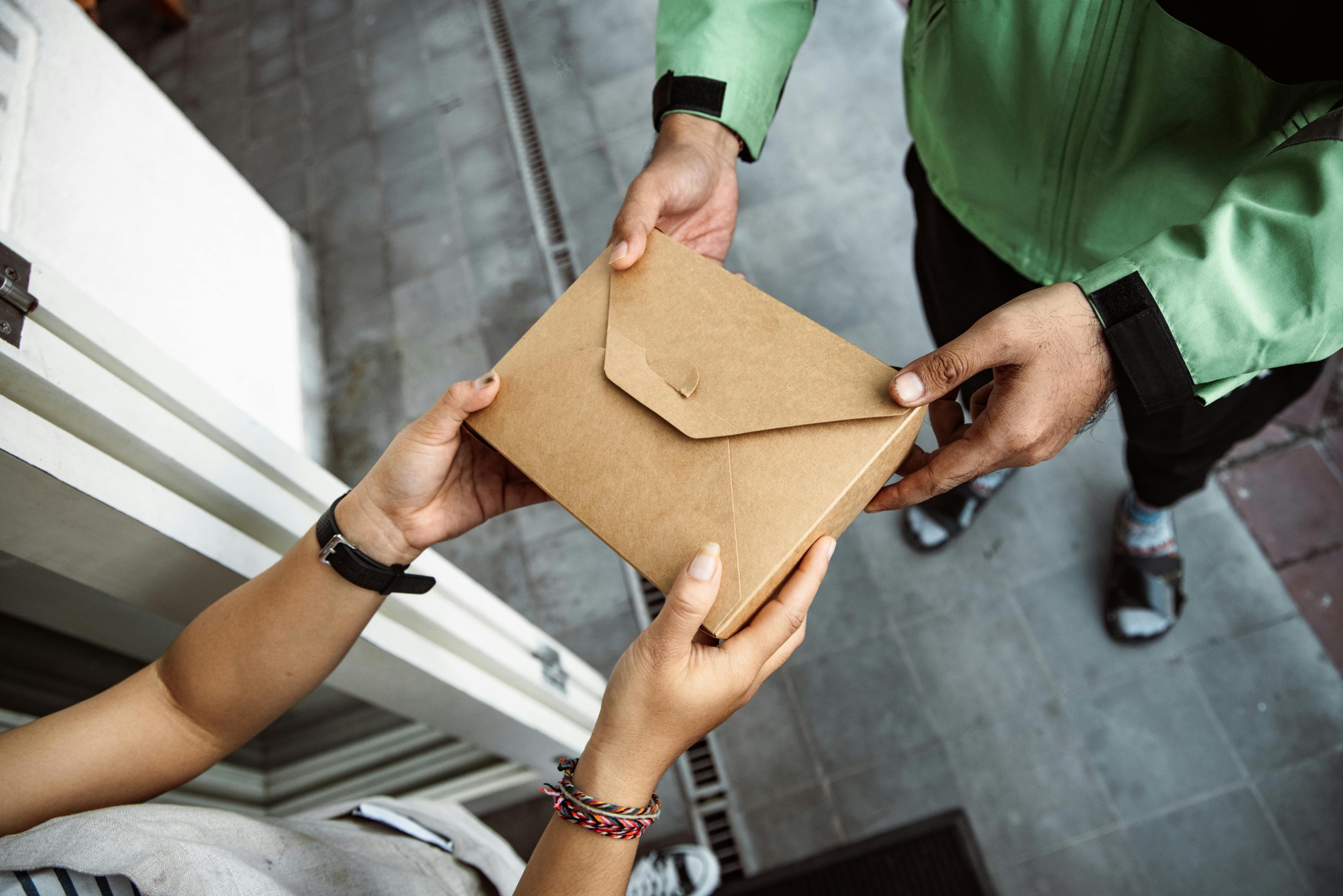 A delivery person hands over a package to a customer outdoors, showing modern service interaction.