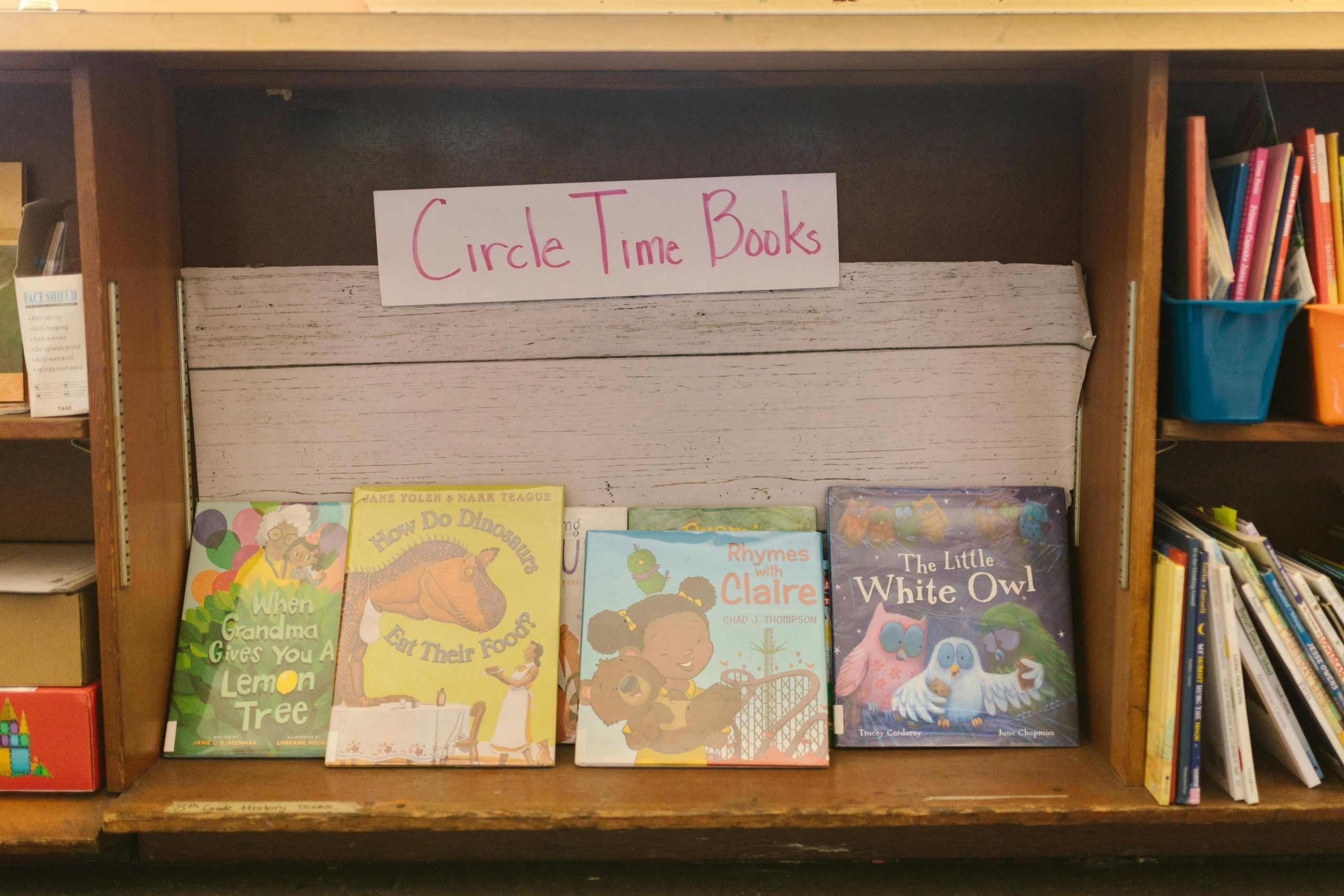 A collection of children's books displayed on a wooden shelf in a library setting.