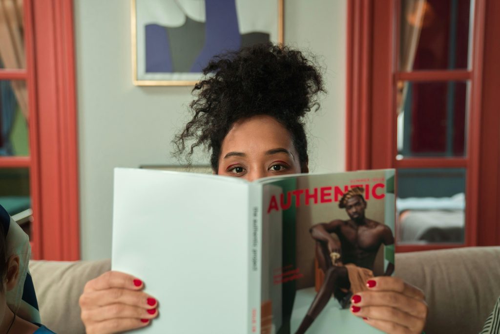 African American woman with curly hair reading a magazine in a cozy indoor setting.